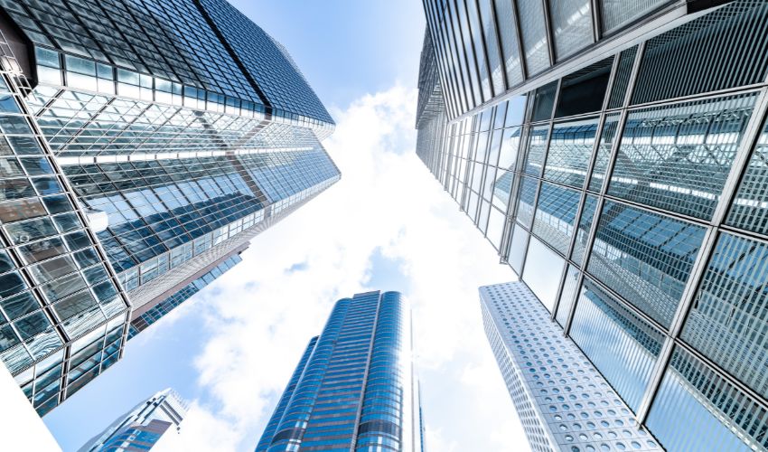 A low-angle view of modern skyscrapers with glass facades reaching toward a partly cloudy sky.